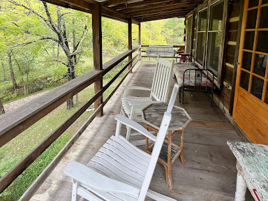Photo of a the Pearl's private, rustic second story porch. Featuring a pair of white rocking chairs, side table, bench against the exterior wall at the mid point, and porch swing at the end.